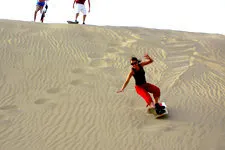 Girl sandboarding sand dunes near Huacachina Lagoon in Ica, 